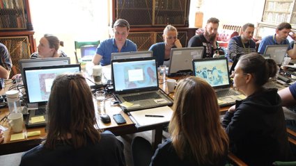 People sat around a table working on laptops with mapping software open. 