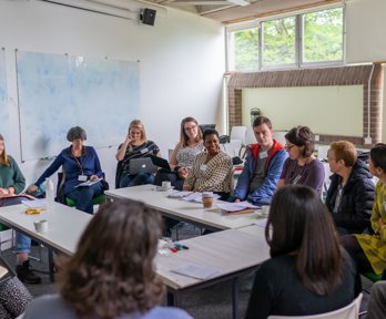 A group of twelve people sit around a table having a discussion. 