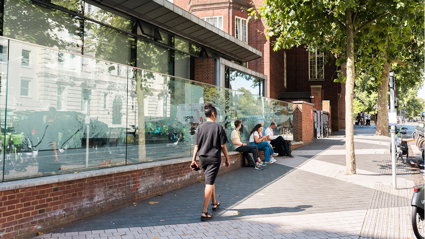 Three people are seated outside the Society's pavilion on a sunny day as one person walks by.