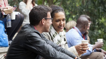 People sat on steps outside talking with cups of coffee.
