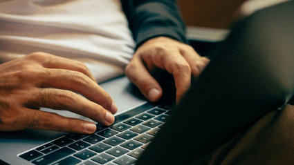 Person typing on a laptop which is resting on their lap.
