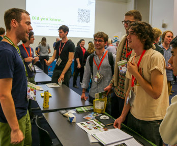 People at a conference networking with an exhibitor standing behind a table.