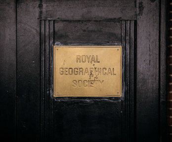 Dark wooden door with a gold-coloured metal sign that says Royal geographical Society. 