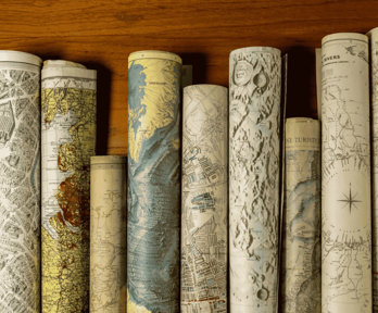 Rolled vintage maps standing upright in a row on a wooden surface.