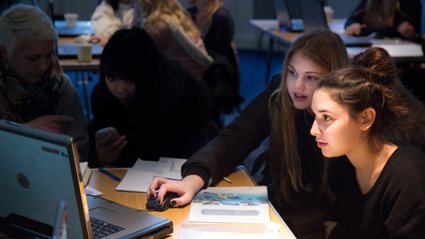 Two school pupils in a class sit looking intently at a laptop.