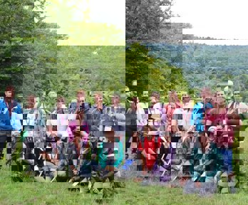 A group of trainee teachers gathered together in the outdoors during a fieldwork day, all smiling and holding geography fieldwork equipment