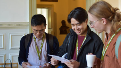 Three people looking at a conference programme and holding coffee cups.