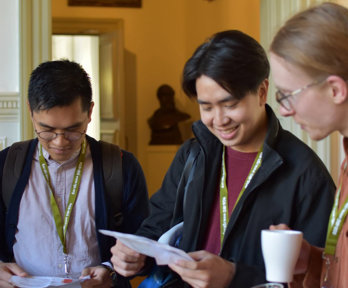 Three people looking at a conference programme and holding coffee cups.