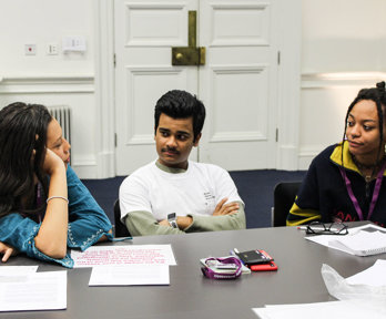 Three people sitting, with one person talking and the two others listening attentively. 