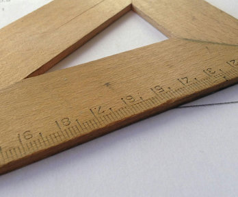 Close up of a brown wooden measuring tool laying on a sheet of paper.