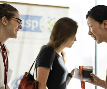 Two people standing across from each other. They are chatting and smiling.