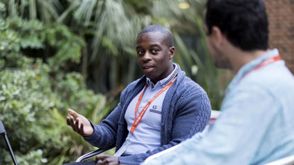Two people having a conversation. One person on the right is sitting with their back to the camera and is blurred out.