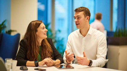 Two people in an office having a conversation and gesturing to one another.