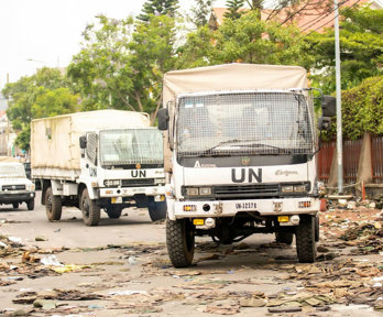 UN trucks driving on a dirty street full of litter.