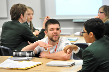 A male geography ambassador crouching down next to a male student, talking to them about geography