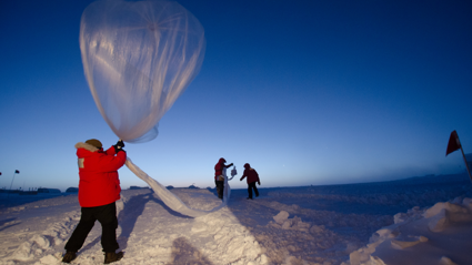 Three people undertake nondescript research in a seemingly artic environment. The snowy landscape stretches as far as the eyes can see